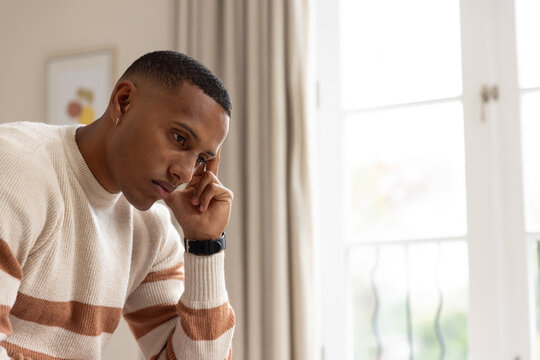 African American man leaning resting head wearing striped sweater black watch near window at home