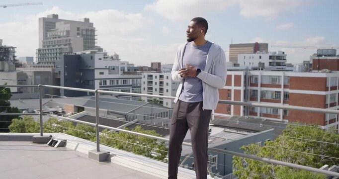 Mid adult man following audio cue, standing on rooftop near railing, checking smartwatch, smiling
