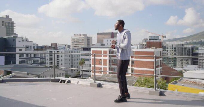 Male walking and stepping on rooftop to music in wireless earbuds, checking device