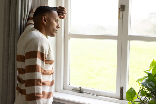 Adult African man standing at window leaning on sill, wearing cream brown knit sweater, copy space