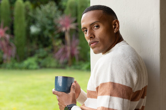 African American man leaning on porch, holding blue mug, wearing sweater and smartwatch, copy space