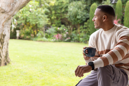 Adult African American man sitting on yard edge holding mug with wristwatch visible, copy space
