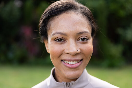 African American woman smiling, facing camera in park wearing gray zip-up jacket and nose stud