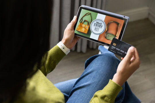 African American woman sitting in green top showing tablet Black Friday badge at home tapping card