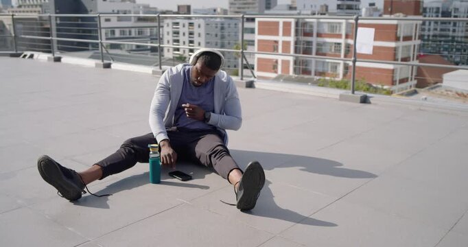 Man putting on headphones after checking phone and tying laces on rooftop preparing workout