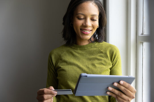 Adult African American woman in green sweater holding folio tablet and checking card at window