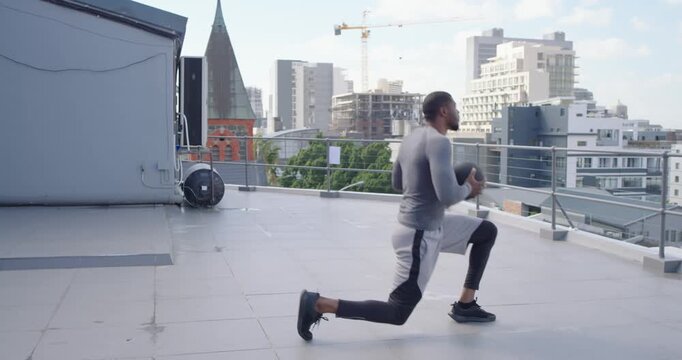 African-American man facing skyline doing lunges with medball on rooftop for training, copy space