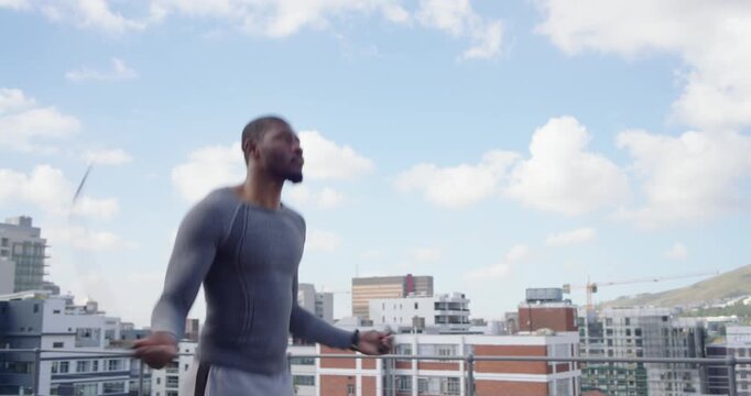 Mid-adult African man swinging rope and jumping for cardio on rooftop, wearing gray top, smartwatch