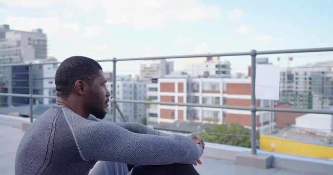 Camera panning, man sitting on rooftop near railing, wearing grey top, holding paper, reflecting
