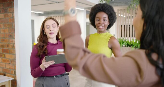 Diverse female coworkers gesturing with red glass, discussing work, using tablet in office lounge