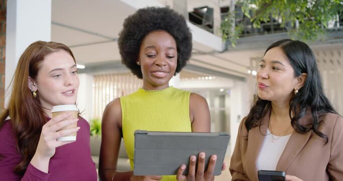Diverse female team leaning in watching center woman tapping tablet and sharing update in atrium