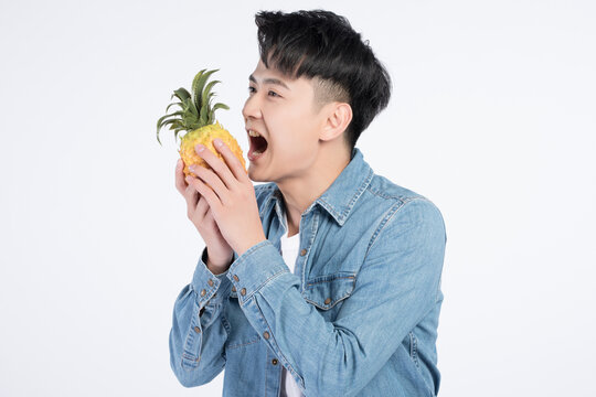 Playful young man pretending to bite a pineapple on light background
