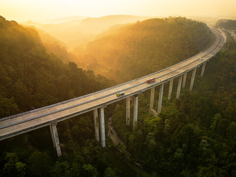 Aerial view of Jalan Tol Bawen - Salatiga crossing a lush forested valley with vehicles on the highway during golden hour in Tengaran, Central Java, Indonesia.