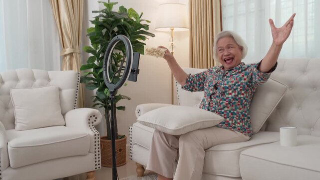 Senior Content Creation: An exuberant senior woman creating content, using a ring light in a cozy living room, bathed in the warmth of natural light.