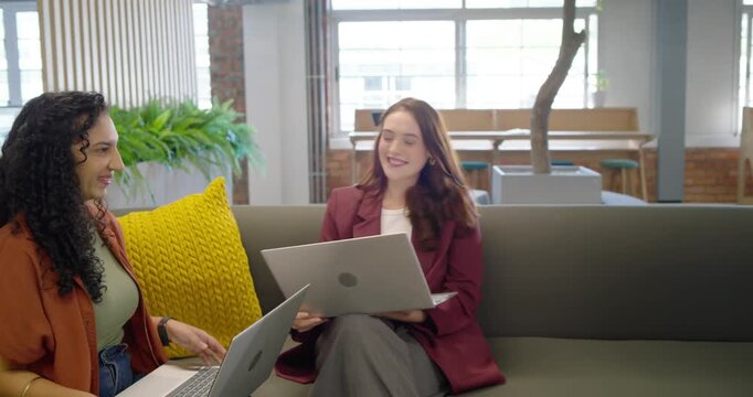 Diverse women in lounge, right woman passing paper touching shoulder, center leading laptop review