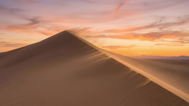 Wind blowing sand across a majestic desert dune at sunset. Golden hour light over a vast arid landscape. Natural erosion process in a beautiful nature scenery.