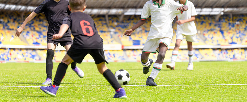 Children Football Tournament Action: Junior Soccer Players Battling on Field with Stands Background