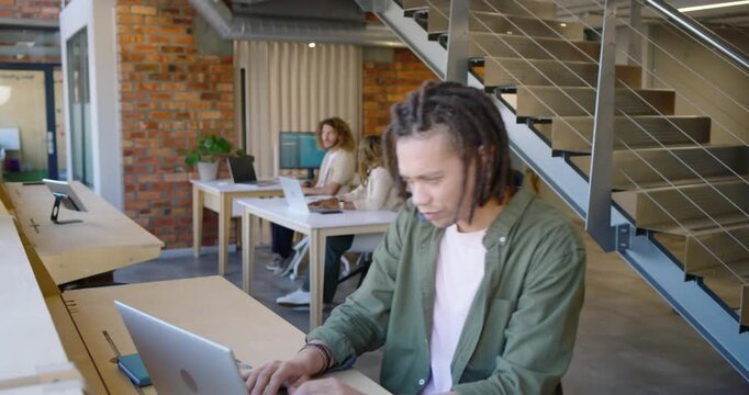 Coworkers watching African American man working on laptop, pausing, smiling in coworking hub