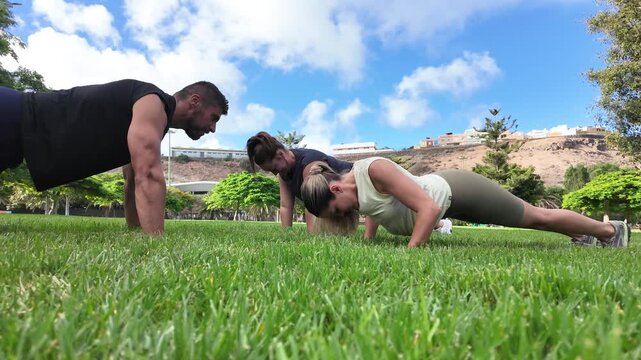 Young fitness friends doing push ups during outdoor workout in a park