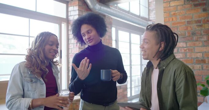 African American team in loft center man starting chat gesturing with mug tablet planning, smiling