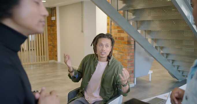 African team meeting with seated man raising hands explaining at desk while colleague with tablet
