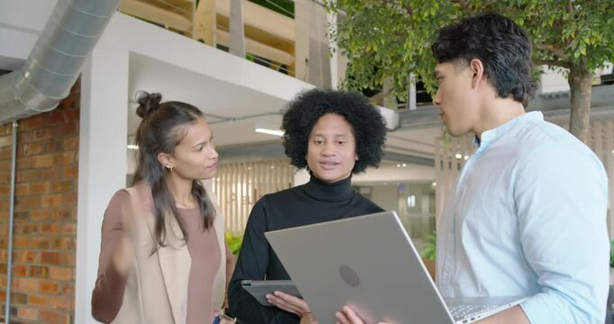 Three coworkers in office, man on right pointing laptop, center holding tablet, discussing project