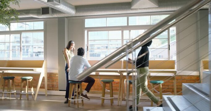 Diverse team watching woman walking across open office carrying laptop and sharing work on counter