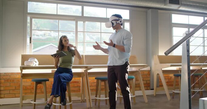 Diverse team woman sitting gesturing tablet man wearing VR headset using controls testing at office