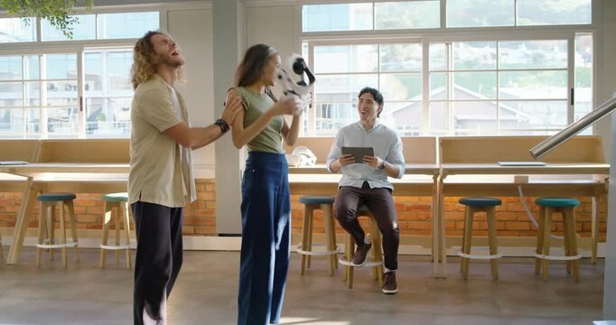 Diverse team in lounge watching woman with white VR headset, man startling her, revealing robot