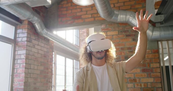 Adult male wearing VR headset and watch manipulating virtual objects while sunlight flaring in loft