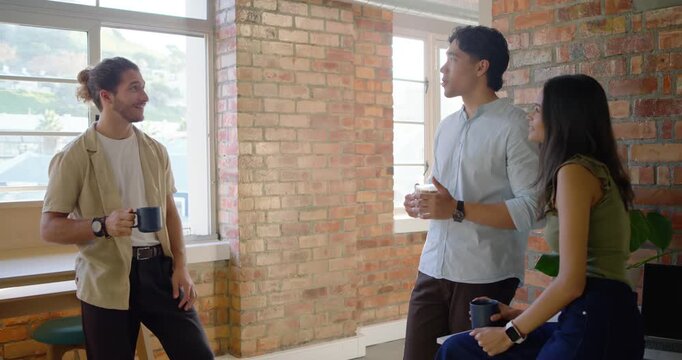 Diverse casual coworkers greeting, clinking mugs and talking during coffee break in loft