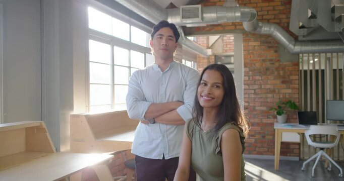 African American woman turning and fixing hair while Asian man posing by windows, sunlight flaring