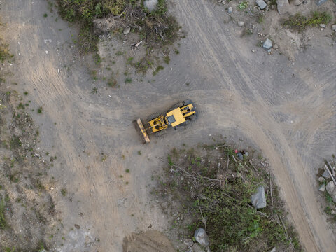 Aerial view of a yellow bulldozer operating in a sand and stone quarry with dirt tracks and rocky terrain in Manisrenggo, Central Java, Indonesia.