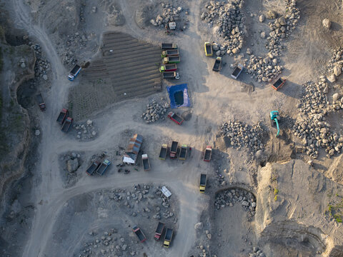 Aerial view of the Sand and Stone Quarry with numerous trucks and an excavator operating in the dusty mining site in Manisrenggo, Central Java, Indonesia.