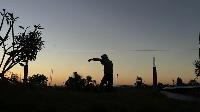 Silhouette of a person doing shadow boxing and martial arts training outdoors during a beautiful golden sunset