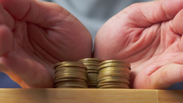 two hands carefully surrounding stacks of coins on a wooden surface, symbolizing investment planning