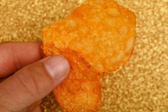 Close-up of a crunchy seasoned potato chip held by a finger against a golden background.