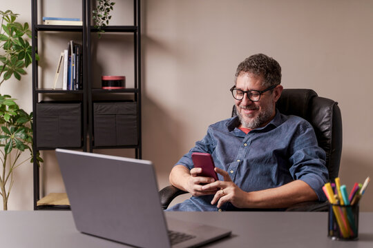 Adult man sits relaxed, smiling, holding phone