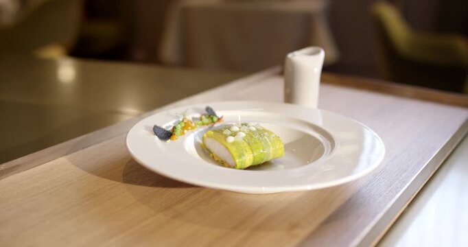 Plated fish dish wrapped in green vegetable leaf rotating on white ceramic plate