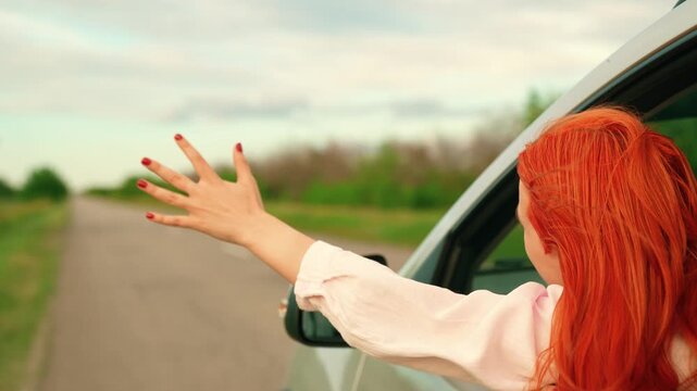 Female student drives car towards wind and adventure. Family trip, teenage girl traveling by car. Young woman passenger catches wind with hands from car window. Family vacation. People travel Auto