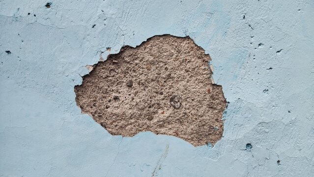 Bogor, Indonesia - June 30,2026
light blue painted wall with a large, irregular hole revealing the rough, sandy brown concrete texture underneath.grunge wall background