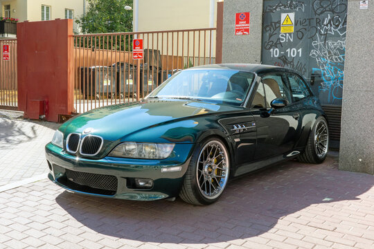 Warsaw, Masovian, Poland - June 26 2026: A dark green BMW Z3 M coupe is parked on a paved street beside a building entrance, captured in daylight.