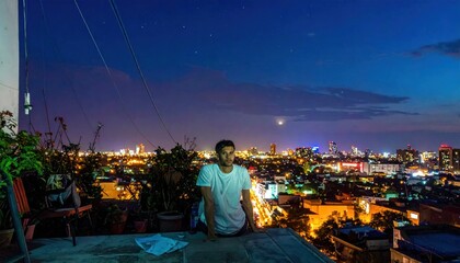 Fototapeta premium Young man in white t-shirt sitting on a rooftop edge gazing at the vibrant night city skyline under a twilight sky with twinkling stars
