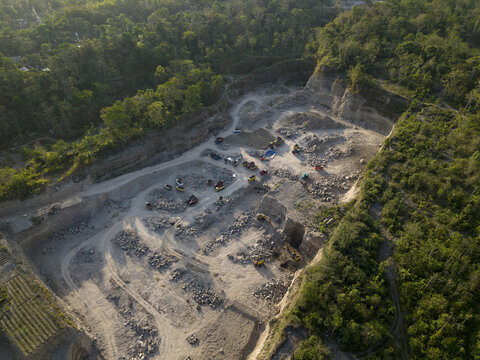 Aerial view of Sand and Stone Quarry with heavy machinery, piles of rocks, and excavation tracks surrounded by lush green forest in Manisrenggo, Central Java, Indonesia.