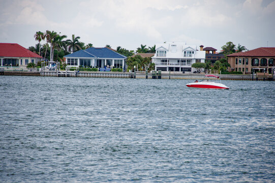 Speedboat cruising along calm coastal waters past waterfront luxury homes, evoking leisure, summer recreation and coastal lifestyle during a relaxed overcast day. View from St. Pete Beach view east.
