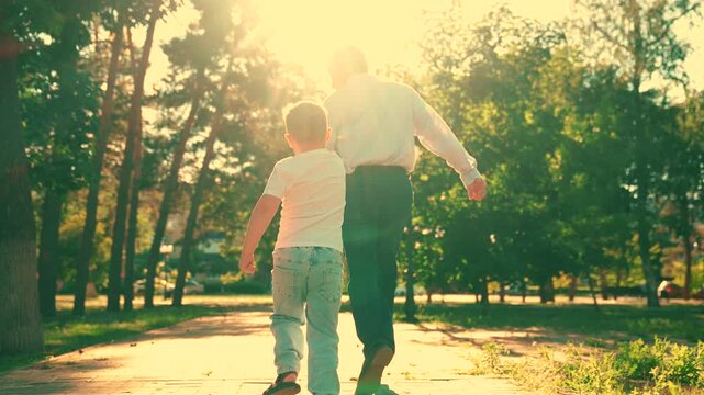 Cheerful little boy runs catch up with dad outside. Young son plays with dad, running together in summer park. Family play. Carefree childhood. Small child has fun outside with dad. Dad laughs kid son