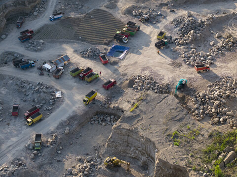 Aerial view of the Sand and Stone Quarry with multiple dump trucks, excavators, and piles of rock in the industrial landscape of Manisrenggo, Central Java, Indonesia.