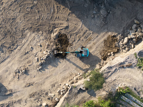 Aerial view of an excavator working in a sand and stone quarry with visible tire tracks and piles of earth in Manisrenggo, Central Java, Indonesia.