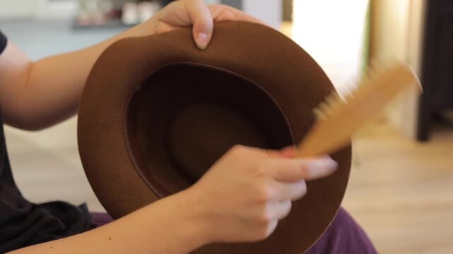 A handheld close-up follows a person brushing a brown felt hat indoors, suggesting mindful care and everyday wardrobe upkeep.