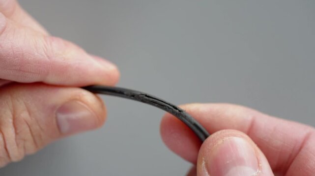 Closeup hands inspecting frayed wire, technician examining cut insulation and exposed copper strands, careful finger manipulation on gray background, precision diagnostic mood,